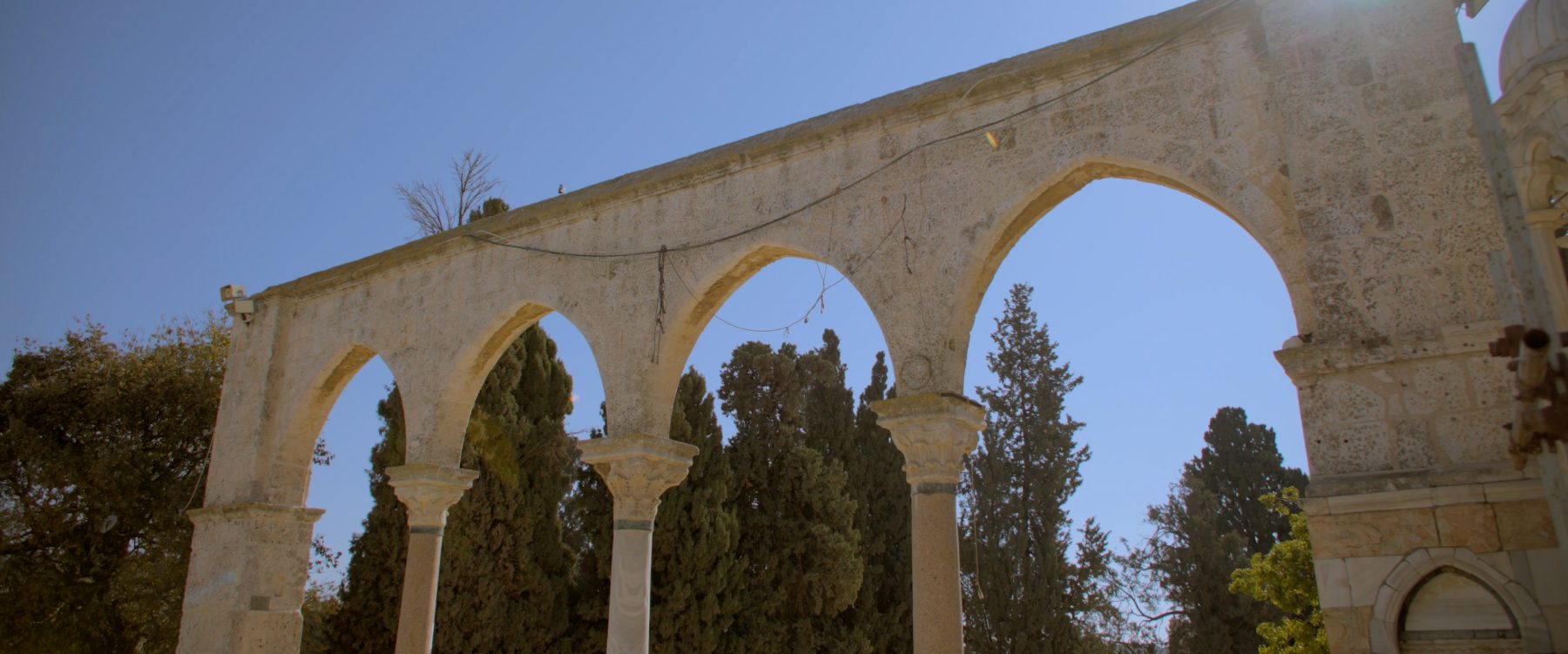 Stone arches within the compound, cypress trees rising behind them